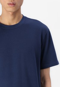 Tengerészkék pamut póló, kerek nyakkal, rövid ujjakkal, sima textúrával. Az anyag enyhén rugalmasnak és könnyűnek tűnik.