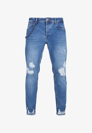 Sinine denimpüksid korraliku lõikega, millel on kulunud plekid, rebenenud äärted ja ketimuuga esikoti piirkonnas.