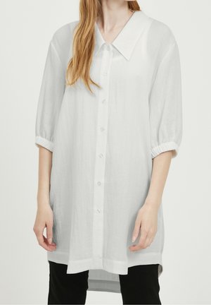 Chemise tunique blanche à boutons en tissu léger, avec un col structuré, des manches demi-longues à poignets élastiques et un ourlet droit.