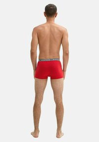 Rote Baumwoll-Boxershorts mit schwarzem Bund, der das Branding zeigt, von hinten betrachtet, mit einer engen, körpernahen Passform.