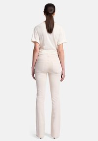 Crème kleurige flare jeans met achterzakken en een middelhoge tailleband, gecombineerd met een losse, kortekleding, lichtgekleurde t-shirt.