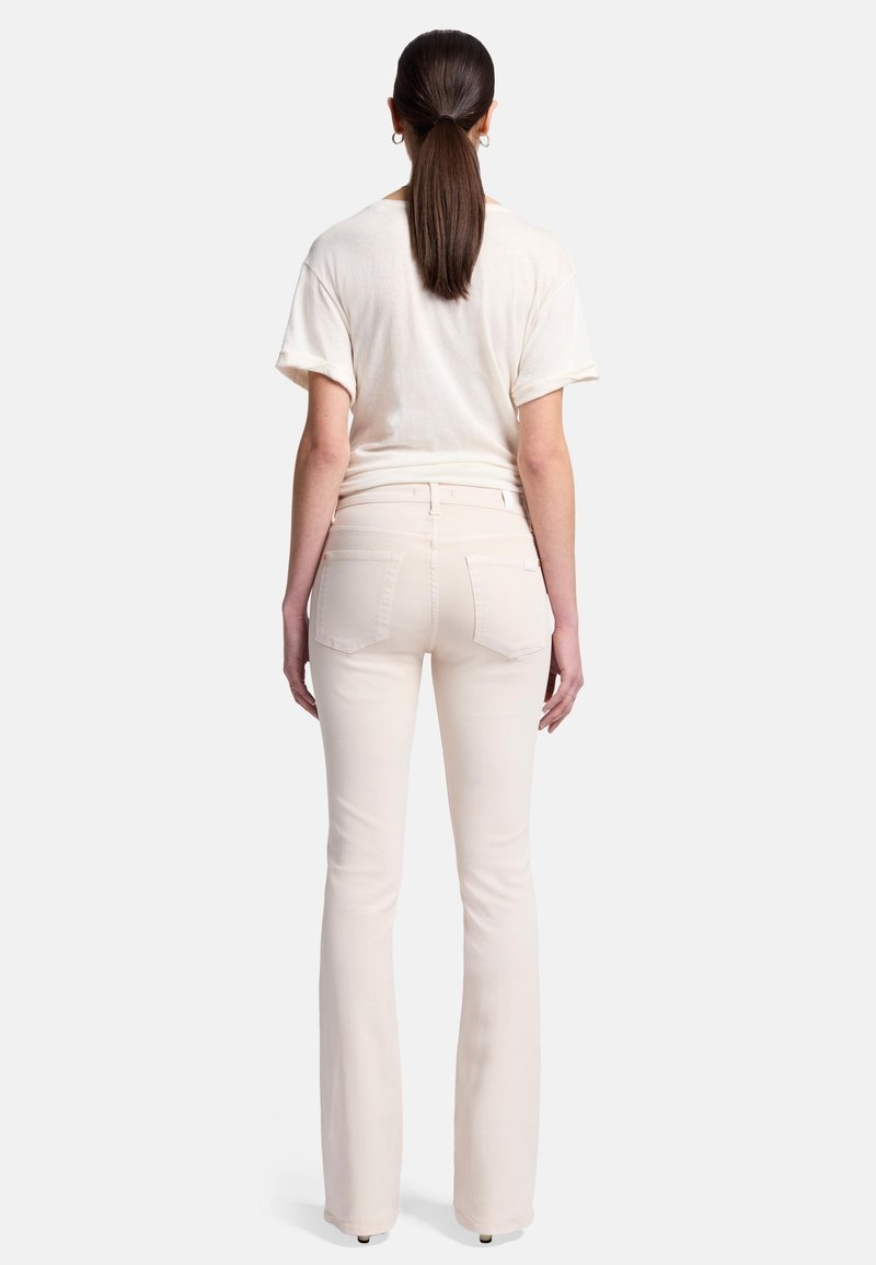 Jeans évasés de couleur crème avec des poches arrières et une taille mi-haute, associés à un t-shirt léger à manches courtes et à coupe ample.