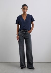 Camiseta de cuello en V de color navy con mangas cortas, combinada con unos jeans negros de pierna ancha. Incluye un cinturón negro y una pulsera blanca texturizada.