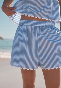 Sinivalkoraidalliset shortsit, joissa on aaltoileva helma, joustava vyötärönauha ja kevyt kangas, sopivat rantavaatteiksi.