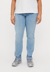 Jeans de mezclilla azul claro con corte recto, que cuentan con un cierre de botón y cremallera. Combinados con zapatillas deportivas grises.