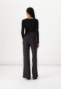 Black long-sleeve top paired with wide-leg, ribbed pants in dark purple with subtle multicolored threads, styled with heels.