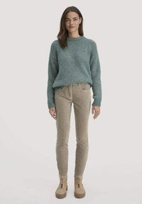 Lichtgroene gebreide trui met een ronde hals, gecombineerd met beige ribfluweelbroek en tan platform enkellaarsjes met ritssluiting.