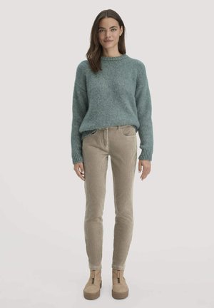 Mintgrüner Strickpullover mit rundem Ausschnitt, kombiniert mit beigen Cordhosen und tanfarbenen Plateauboots mit Reißverschlussdetails.