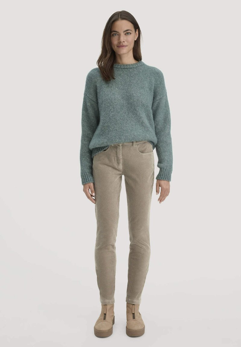 Lichtgroene gebreide trui met een ronde hals, gecombineerd met beige ribfluweelbroek en tan platform enkellaarsjes met ritssluiting.