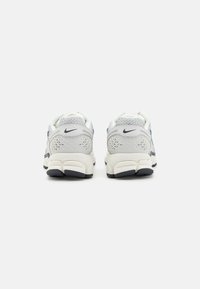 Scarpe sportive bianche e grigie con materiale in rete, accenti a motivo e suola imbottita. Presenta un logo sul retro e un design testurizzato.