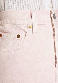 Jeans in denim rosa chiaro con una trama sottile, dettagli in metallo color oro sulle tasche e una vita pulita con chiusura a bottone.