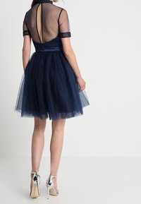 Abito in tulle navy con corpetto trasparente, maniche corte e schiena a chiave, accentuato da una cintura in satin e scarpe con tacco alto argentate.