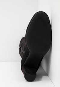 Botín de ante negro con una suela de goma negra lisa, cierre de cremallera lateral y punta redondeada, que muestra una superficie texturizada.