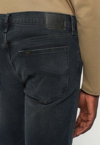 Temno sive denimske hlače, ki vsebujejo usnjeni logotip "Lee", podrobnosti na zadnjih žepih in prilega silhueto. Mehka tekstura, klasičan kroj.