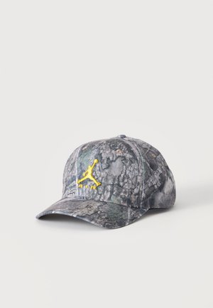 Czapka bejsbolowa w kamuflażowy wzór z żółtym wyszywanym logo Jumpman oraz napisem „Air” z przodu na jednolitym tle.