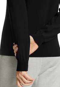 Schwarzer Strickpullover mit langen Ärmeln, gerippten Bündchen und einer glatten Textur. Grauer Stoff ist an der Taille sichtbar und zeigt eine taillierte Silhouette.