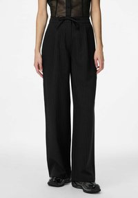 Pantalon large noir à fines rayures, avec une taille à cordon de serrage et une texture lisse. Présente une coupe décontractée et un design élégant.