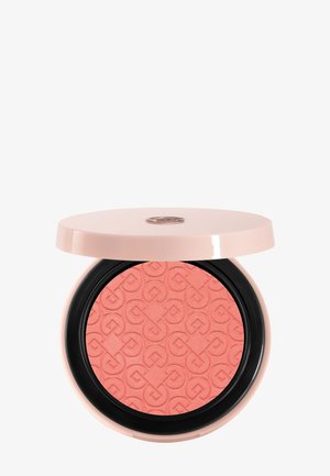 Compact round coral blush with embossed geometric pattern, housed in a pale pink case with a black inner ring and a partially open lid.