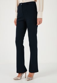 Navy blue tailored trousers with a smooth texture, featuring belt loops and a front zipper closure. Paired with patterned high heels.