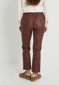 Pantalones de cuero sintético marrón con un ajuste ceñido, que presentan dos bolsillos traseros y una textura suave. Combinados con zapatillas de estampado de leopardo.