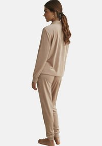 Ensemble de vêtements d'intérieur en velours beige comprenant un haut à manches longues et un pantalon assorti, tous deux avec des poignets côtelés, une texture douce et une coupe décontractée.