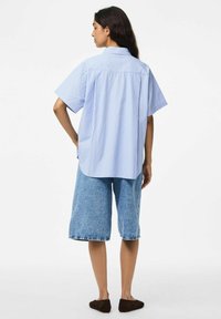 Gaiši zils, svītrots, īsām piedurknēm krekls ar brīvu piegriezumu, pārī ar līdz ceļiem garām džinsu šortiem un tumšiem čības.