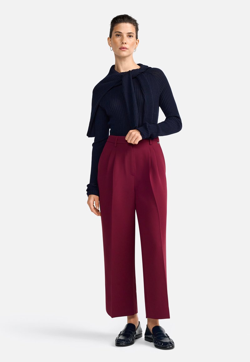 Marineblauwe geribbelde trui met een oversized kraag, gecombineerd met hoog in de taille gesneden bordeauxrode broek met plooien, en zwarte instappers.