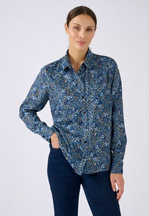 Camisa azul de botones con manga larga, con un patrón de pequeñas flores y hojas en diferentes tonos de azul y verde.
