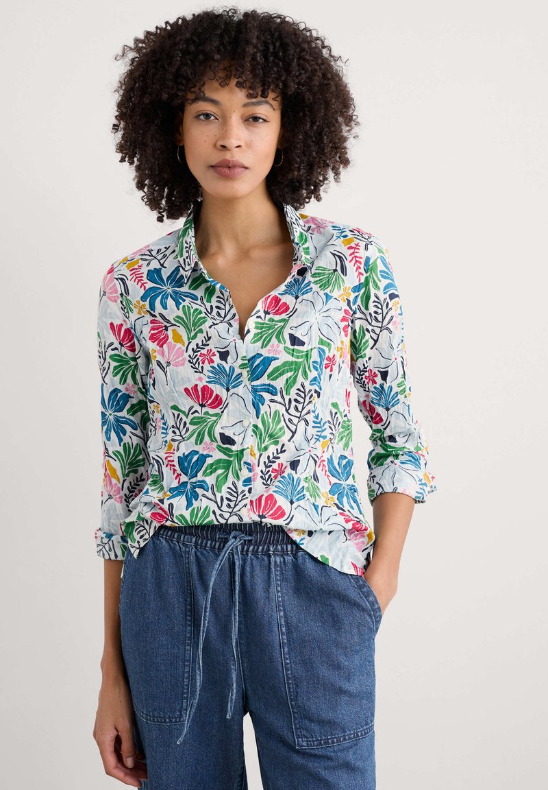 Chemise à boutons florale en tissu léger. Présente des imprimés colorés de feuilles et de fleurs, avec un col et des manches retroussées.