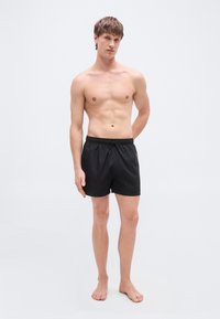 Μαύρο μαγιό σορτς με ελαστική μέση και κορδόνι. Απαλή υφή υφάσματος, μήκος μέχρι το γόνατο, μίνιμαλ στιλ, χωρίς ορατά σχέδια ή διακοσμητικά.