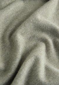 Lichtgroene gebreide stof met een gladde textuur, met subtiele variaties en plooien, wat wijst op een zacht en flexibel materiaal.