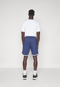 Calções atléticos azuis com um acabamento branco, feitos de um tecido leve, combinados com uma t-shirt branca simples e ténis pretos.