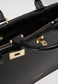 Borsa Michael Kors in pelle nera con hardware dorato, manici strutturati e tasca interna con zip visibile.