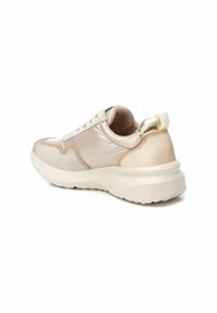 Zapatillas de deporte en beige claro con acentos metálicos dorados, superficies lisas y texturizadas, cuello acolchado y una suela blanca gruesa.