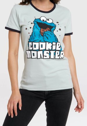 Lichtblauw T-shirt met zwarte rand met Cookie Monster die een koekje eet en de tekst "COOKIE MONSTER" in grote blokletters.