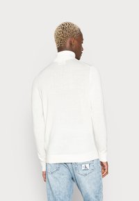 Hvid, let sweater med høj krave, ribbede manchetter og kant. Blevet båret med lyse vaskede jeans. Glat tekstur, slim fit design.