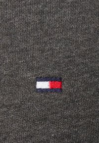 Tessuto lavorato a maglia grigio scuro con un piccolo logo ricamato che presenta strisce orizzontali rosse, bianche e blu su uno sfondo blu navy.