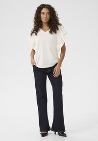 Blusa bianca di cotone con maniche a volant abbinata a jeans a zampa d'elefante blu scuro. Scarpe nere con dettagli decorativi in metallo.