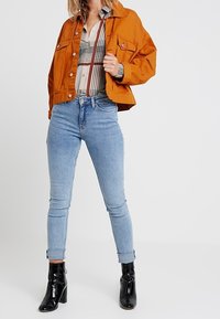 Orange denim jacket, plaid shirt with lines, light blue skinny jeans, and black heeled ankle boots. Visible buttons and a structured fit.