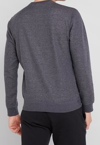 Sudadera larga gris de manga larga hecha de tejido suave, con cuello redondo, puños y bajo acanalados, y una textura sutil.