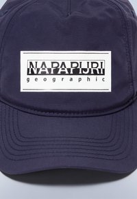 Marineblauwe pet van gestructureerde stof met een rechthoekig wit logo met zwarte tekst "NAPAPIJRI" en "geographic" in een kleiner lettertype.