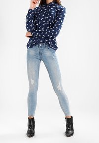 Námořnická modrá košile s dlouhým rukávem a bílým zvířecím potiskem, spárovaná se světle modrými roztrhanými skinny džíny a černými kotníkovými botami s kovovými detaily.