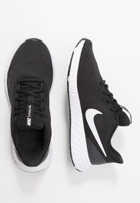 Scarpe da corsa nere Nike con tomaia in rete texturizzata, suola bianca, lacci neri e un grande logo Swoosh bianco sui lati.