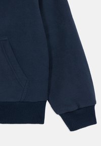 Navy fleece genser med kengurulomme, ribbede mansjetter og glatt tekstur. Stoffet er mykt og varmt.