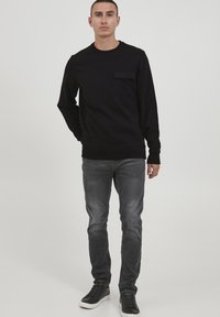 Schwarzer Hoodie mit einer Brusttasche, rundem Halsausschnitt und langen Ärmeln, kombiniert mit grauen Slim-Fit-Jeans und schwarzen Sneakers. Schlichtes Design.