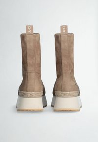 Stivaletti in suede marrone con tacco a blocco, caratterizzati da un design testurizzato e un'etichetta logo prominente sul retro. Motivo decorativo sulla suola.