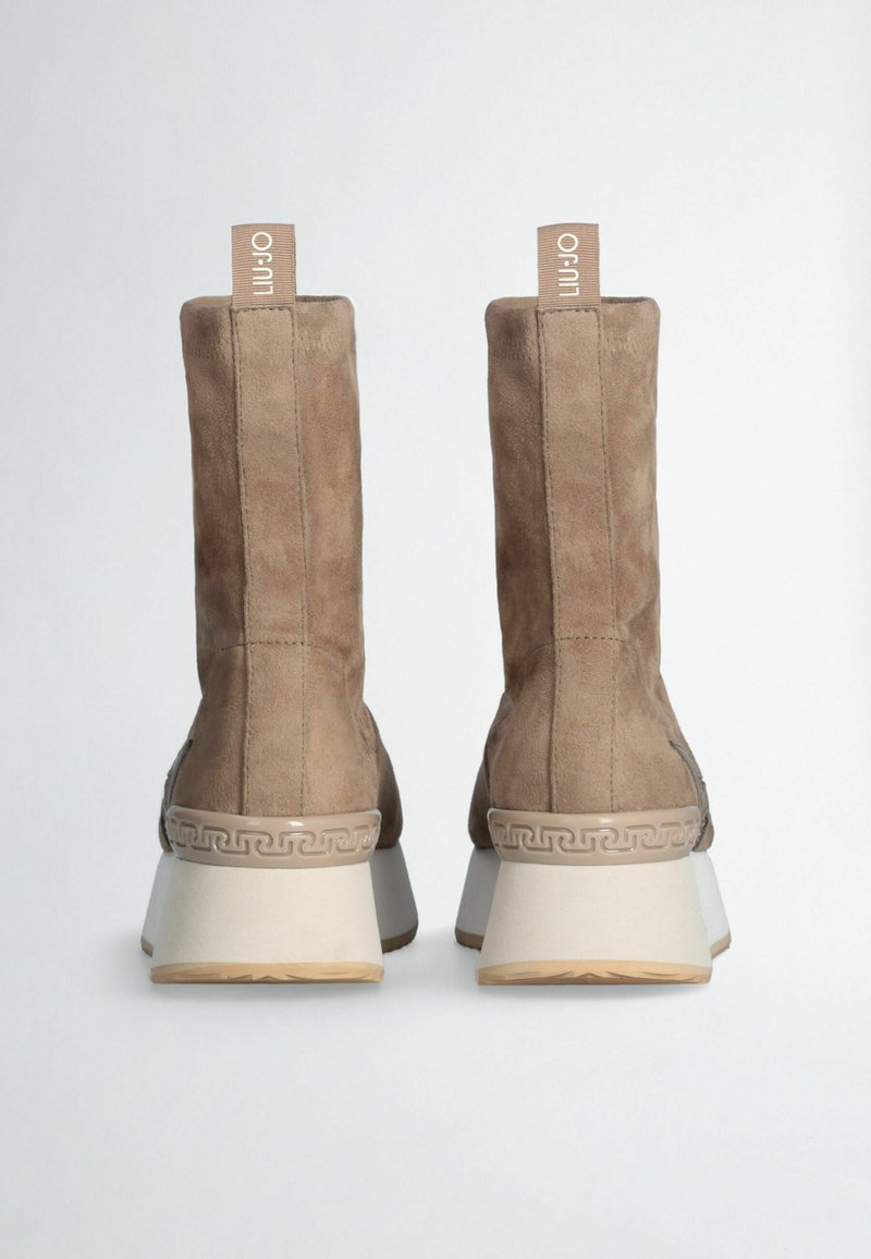 Bottines en suede marron avec un talon carré, présentant un design texturé et une étiquette de logo bien visible à l'arrière. Motif décoratif sur la semelle.