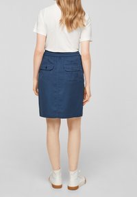 Marinblå bomullskjol med elastisk midja, med två bakfickor med knappar, knälång, slät textur.