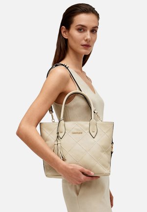 Borsa tote in pelle trapuntata beige con rifiniture nere, doppio manico e dettaglio a nappe. Presenta un logo dorato sulla parte frontale.