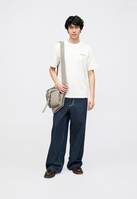 Casual outfit med en hvid t-shirt med rød tekst, marineblå bukser med smalle striber og vide ben samt en grå crossbody taske. Brune sko fuldender looket.
